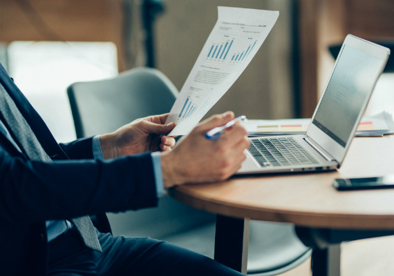 person with a laptop and a reporting document in hand